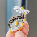 Primo piano di una graziosa spilla in smalto a forma di riccio con margherita bianca - Fiore Bianco