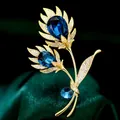 Elegante broche de flor dorada de lujo con cristal azul real y micropavé de circonitas - B598