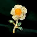 Exquisito broche de flor dorada con perla central naranja y hojas de circón verde - B613