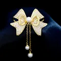 Elegante broche de lazo dorado con circonitas micropavé y gotas de perlas blancas - B483