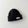 Detail showing the thick knit texture and branded label of a black winter beanie hat - Kids / Black
