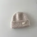 Close-up detail of a soft beige baby ribbed knit winter beanie with a stylish label - Kids / Beige