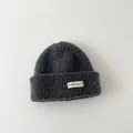 Close-up detail of a dark grey kids' knitted beanie featuring a fabric patch label. - Kids / Dark Gray