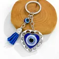 Detail of heart-shaped evil eye keychain with blue tassel on a wood block. - Silver Heart Blue Tassel Motif (8425)