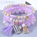 Primo piano di un set di quattro bracciali di perline viola con ciondolo happy e nappa viola. - Viola