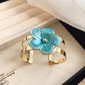 Detailed view of an island style gold cuff bracelet with a vibrant blue enamel flower detail. - Bangle / Blue