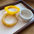 Detailansicht von leuchtend gelben und marmorierten weißen Harzarmbändern in einer Holzschale - 30# (3-teiliges Set)