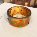 Primo piano di bracciale in resina ambrata sfumata con strass multicolori. - Stile Zirconia / Marrone Ambra