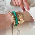 Dettaglio di bracciale in resina marmorizzata verde e polsino floreale dorato al polso - Set di 3 pezzi / Oro e Blu