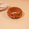 Vista detallada de un brazalete de resina marrón rojizo con detalles de ojales retro - Estilo Remache Café