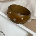 Vista detallada de un brazalete de resina ámbar con adornos de tachuelas metálicas plateadas - Café Oscuro