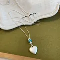 Gros plan d'un collier avec pendentif cœur en argent mat et perles bleues et blanches - 6# Style Coeur