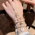 Primo piano di braccialetti dorati con ciondoli a tema oceano, stelle marine e conchiglie - 28# Braccialetto / 5 Pezzi / Oro & Bianco