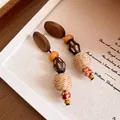 Close-up of ethnic earrings with wood beads, raffia woven balls and silver needle studs - Style 3 / Brown