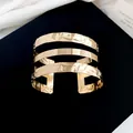 Detailopname van een brede gouden manchetarmband met een unieke gehamerde textuur. - Meerlaagse Geplooide Stijl / Goud