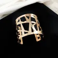 Gedetailleerd close-up beeld van een gepolijste goudkleurige manchetarmband met geometrisch patroon - Geometrische Holle Stijl / Goud