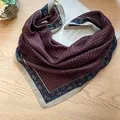 Detailed view of a vintage burgundy square scarf with ethnic patterns on a wooden surface. - Coffee Polka Dot