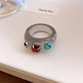 Macro-weergave van een grijze harsring met kleurrijke strassteentjes op een kaart. - Zetting met drie diamanten / Grijs En Rood