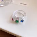 Detailopname van een heldere harsring met levendige veelkleurige vierkante kristallen. - Zetting met drie diamanten / Wit-Groen