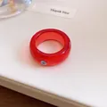Macro-opname van een rode harsring met een klein paars strassteentje op een witte achtergrond - Rood