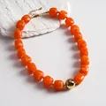 Detailed close-up of a chunky orange marbled acrylic bead necklace with gold ball accent - Necklace / Gold-Orange