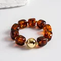 Close-up of amber acrylic bead bracelet with a central gold metallic spherical accent - Bracelet / Gold Brown