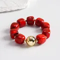 Macro view of marbled red acrylic square beads paired with a shiny gold orb on a bracelet. - Bracelet / Gold-Red