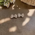 Close-up detail of elegant transparent beaded bow-shaped earrings on a rustic wooden surface - Stud Earrings / 925 Silver Earring Post / White