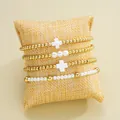 Set of 4 gold and white beaded elastic bracelets with cross charms on a display pillow. - 6358901HB / CCB