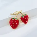 Detailed view of a fashionable red enamel strawberry brooch with glossy gold-tone accents - 2 Strawberries