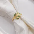 Détail d'un rond de serviette en métal doré avec strass verts en forme de feuille - Style Zircon Vert / Or