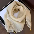 Detailansicht eines eleganten beigen Seidenquadratschals mit silbernen Streifen und Goldanhängern - Paillette Champagner