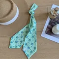 Detailansicht eines hellgrünen Satin-Seidenschals mit Blumenmuster neben einem Strohhut - Grün Floral