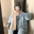 Frau trägt eine hellblaue Daunenjacke und einen beigen Strickschal aus Wollmischung. - Beige Grobe Wollmischung