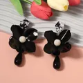 Close-up of black metal flower earrings with white pearl center and teardrop pendant. - Black