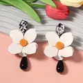 Close-up of elegant white flower earrings with black teardrop pendants and orange centers. - White