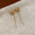 Elegant gold-plated butterfly threader earrings displayed on a beige knitted background - 48 Earrings - Gold