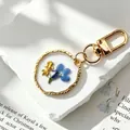 Macro view of handmade resin keychain featuring real blue dried flower and gold fish charm - Blue Flower