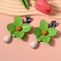 Close-up detail of vibrant green metal flower earrings featuring white teardrop pendants - Emerald Green