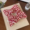 Elegant close-up of a red gingham heart scrunchie with a lace bow on a vintage book - Square Scarf Scrunchie / Red White Plaid