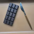 Realistic dark chocolate bar squishy toy for stress relief with table knife prop detail. - Chocolate Bar / Dark Brown
