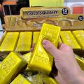 Detailaufnahme einer Hand, die ein realistisches goldbarrenförmiges Squishy-Spielzeug hält - Backsteindesign / 12er Set / Gold