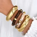 Chunky stackable acrylic and gold-tone metal bangle set stylishly worn on model's wrist - Mix and Match Twisted Bangle (6620601HB) / Four-Piece Set / Gold Brown White Twisted Combo