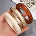 Set of three chunky acrylic and gold-tone bangles in white marble and amber finish. - 3-Piece Thick Round Bangle Set (6699801) / Marble White/Gold/Amber