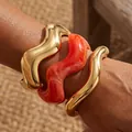 Elegant statement wavy acrylic and gold-toned cuff bangle set shown on model wrist - 3-Piece Wave Open Bangle Set (6781101HB) / Gold and Orange Marble