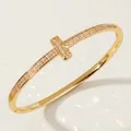 Elegant gold-toned T-shape bangle featuring pavé cubic zirconia and a hinged closure. - Gold Zirconia Commute Bangles BS-J5520G