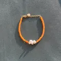 Gedetailleerde opname van een boheemse handgemaakte armband met oranje kralen en schelp. - Oranje Gefacetteerde Kraal Stijl (P) / 17+3cm