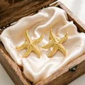 High-quality close-up of gold starfish stud earrings resting on cream satin inside a wooden box - Starfish Stud Style