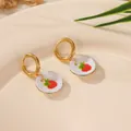 Close-up of 18K gold plated stainless steel hoop earrings with ceramic strawberry charms. - Strawberry Plate