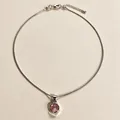 Gros plan d'un collier en argent avec un pendentif rond en calcédoine rose sur fond texturé. - Rose
